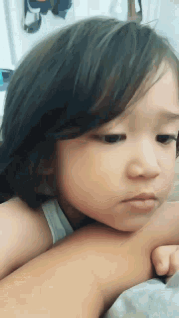 a little girl with long hair is laying on someone 's lap and looking at the camera .