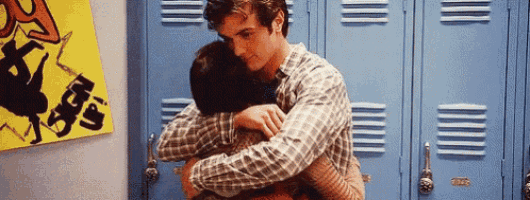 a man is hugging another man in front of blue lockers in a locker room .