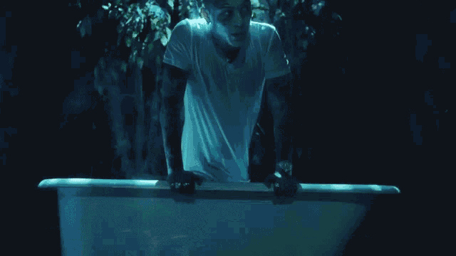 a man in a white shirt is standing in a bathtub in the dark