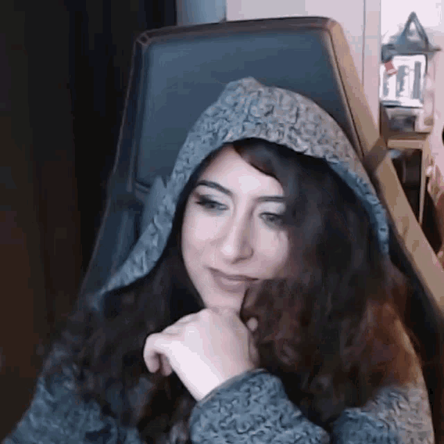 a woman wearing a hooded jacket is sitting in a chair .