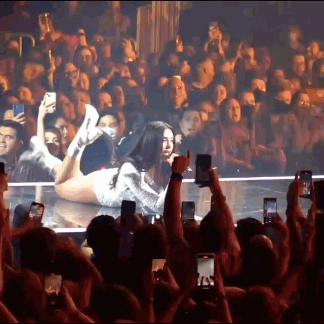 a woman is laying on a stage in front of a crowd of people taking pictures with their phones