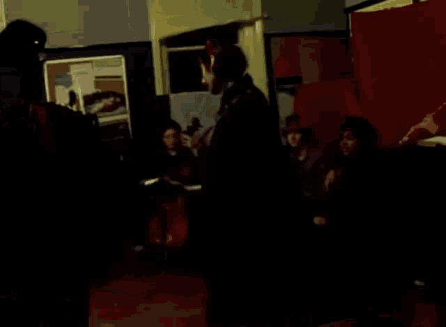 a group of people are standing in a dark room with a red wall behind them