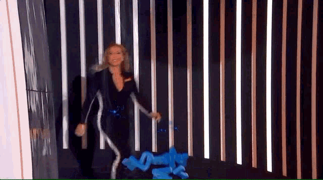 a woman in a black suit is walking through a maze of lights
