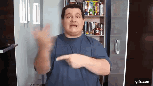a man in a blue shirt is making a funny face while pointing at something .