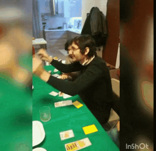 a man sits at a table with a green table cloth and playing a game of cards