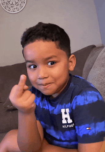 a young boy wearing a blue striped shirt with the letter h on it giving the middle finger