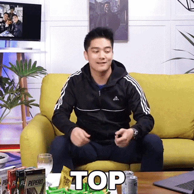 a man is sitting on a yellow couch with the word top above him .