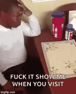 a man is sitting at a desk with his hand on his forehead and says " fuck it show me when you visit " .