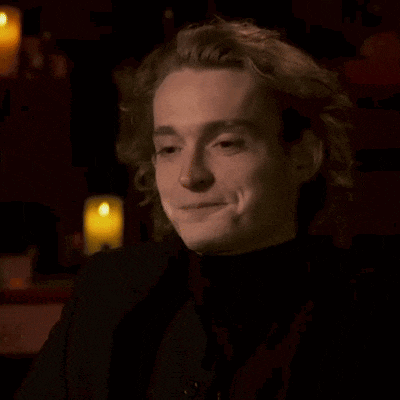 a young man with curly hair is smiling in a dark room .