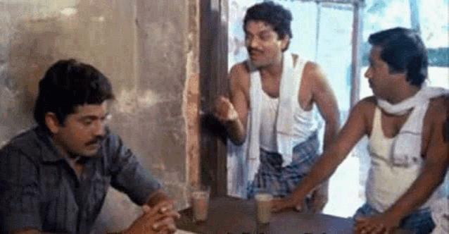 a group of men are sitting at a table talking to each other in a room .