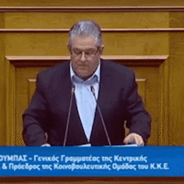 a man in a suit is giving a speech at a podium in front of a sign that says sympas