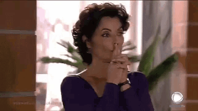 a woman in a purple shirt is covering her mouth with her hands and looking at the camera .