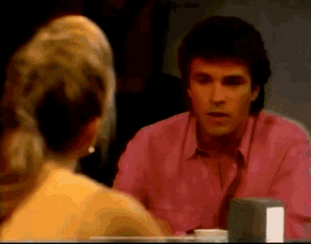 a man in a pink shirt and tie is talking to a woman