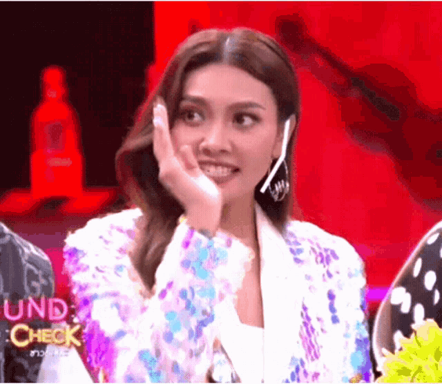 a woman in a sequined jacket is smiling and covering her mouth with her hand