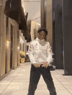 a man wearing a white adidas jacket is dancing in a hallway