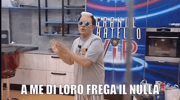 a man wearing sunglasses is standing in front of a sign that says ' a me di loro frega il nulla '