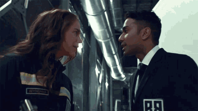 a man and a woman are looking at each other and the man has a badge that says b9