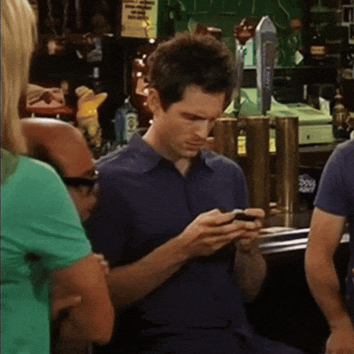 a man in a blue shirt is looking at his cell phone