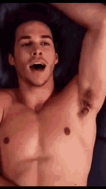 a shirtless man is laying on a bed with his mouth open and his arms outstretched .