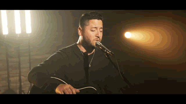 a man is singing into a microphone while playing an acoustic guitar