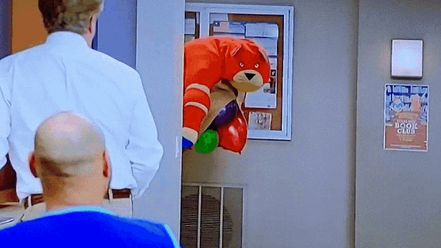 a bald man is looking at a stuffed animal with boxing gloves on