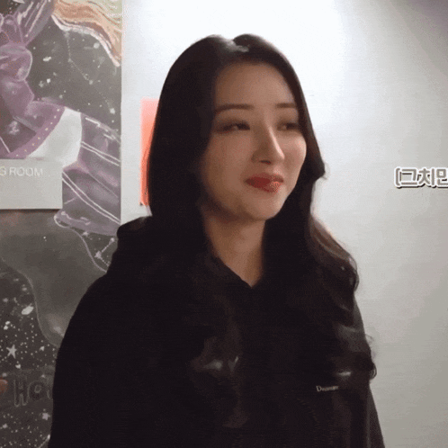 a woman in a black hoodie stands in front of a poster that says groom