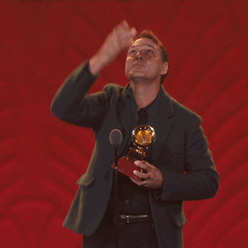 a man in a green jacket holds a trophy in front of a red background