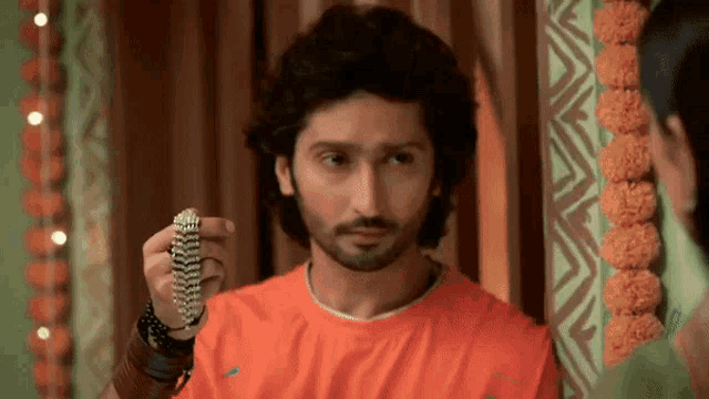 a man in an orange shirt is holding a bracelet in his right hand