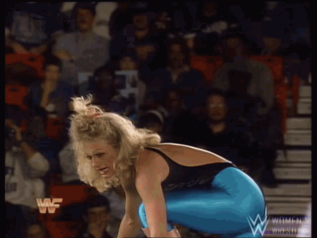 a woman in a black top and blue pants is kneeling down in front of a crowd with the letters wf on the screen