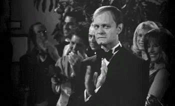 a man in a tuxedo is clapping his hands in front of a crowd .