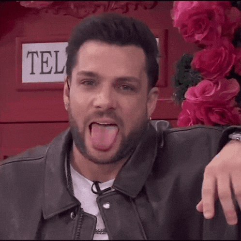 a man in a leather jacket is sticking his tongue out in front of a phone booth .