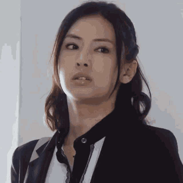 a woman is wearing a black jacket and a white shirt and looking at the camera .