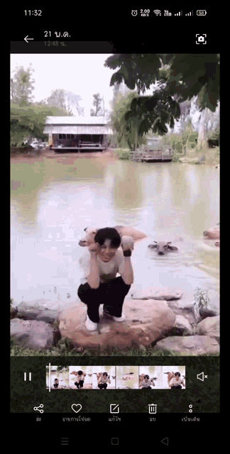 a phone screen shows a man kneeling on a rock in front of a lake