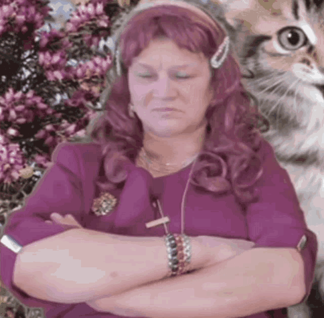 a woman with pink hair is sitting with her arms crossed and a cat behind her