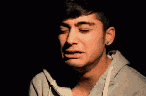 a young man with blue ear piercings is crying with his eyes closed