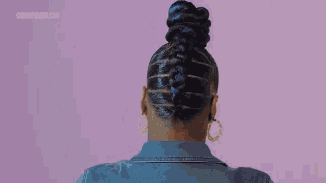 a woman wearing hoop earrings and a braided bun against a purple background with cosmopolitan.com written on the bottom