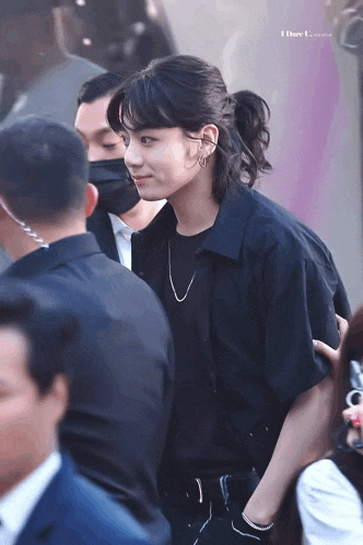 a man wearing a black shirt and a ponytail is standing in a crowd of people .