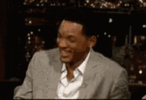 a man in a suit is smiling while sitting in a dark room .