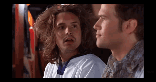 a man with long hair is sitting next to another man with a beard