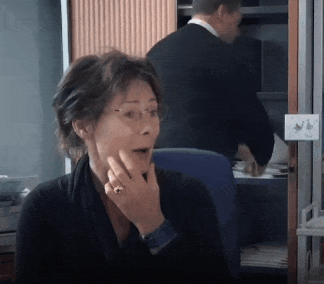 a woman with a surprised look on her face is sitting in front of a man in a suit