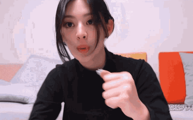 a woman in a black shirt is holding something in her hand with a foreign language written in the corner