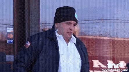 a man wearing a black jacket and a black beanie is standing in front of a visa sign