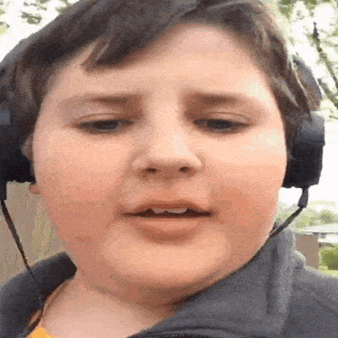 a boy wearing headphones looks at the camera with a serious look on his face