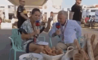 a man and a woman are sitting at a table talking into microphones while eating food .