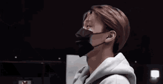 a man wearing a black face mask and a gray hoodie is standing in a dark room .