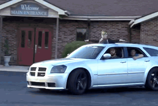 a silver dodge magnum is parked in front of a building that says welcome main entrance