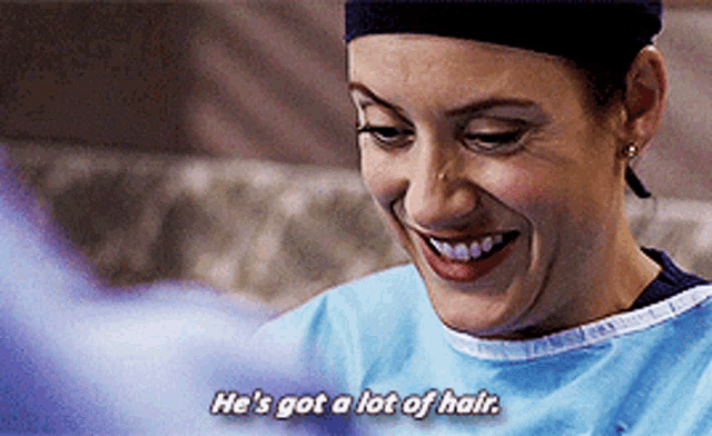 a woman in a surgical gown smiles and says he 's got a lot of hair