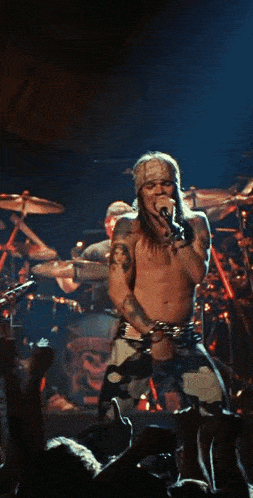 a shirtless man singing into a microphone with a bandana on his head