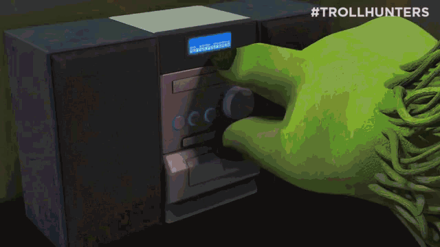 a green hand is pressing a button on a device with #trollhunters written on the bottom