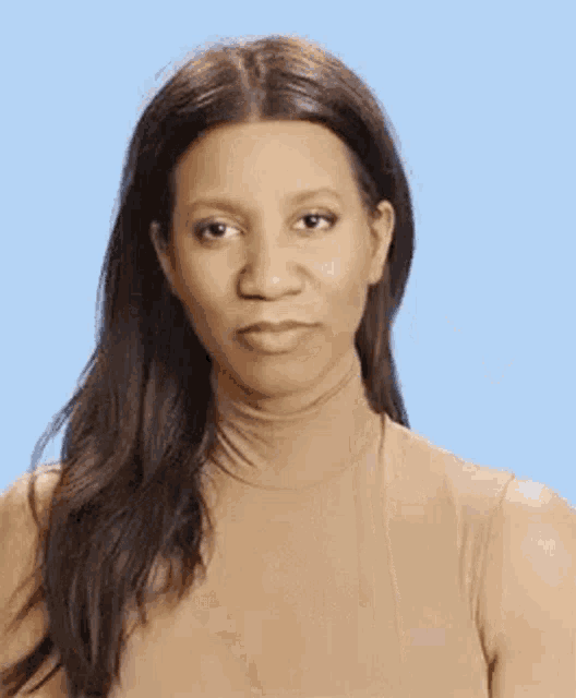 a woman wearing a tan turtleneck is making a funny face .